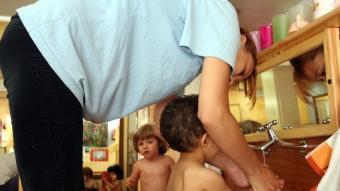 Una educadora ajuda un infant a netejar-se en una escola bressol municipal de Barcelona MARTA MARTÍNEZ