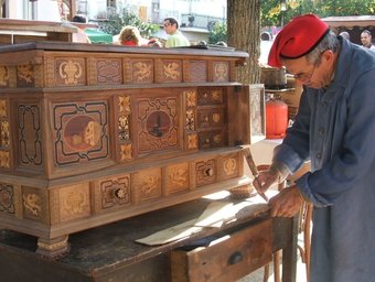 Un artesà treballant en un moble de fusta, a la fira.  AJ. LES PLANES D'HOSTOLES