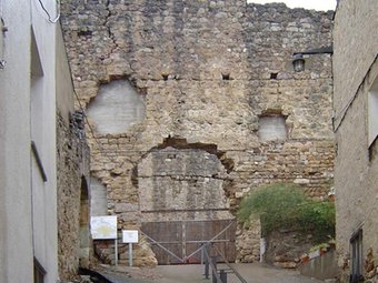 Un tros del mur exterior del castell que es barreja amb cases i carrers EL PUNT