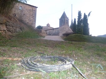 La casa de l'afectat i l'església de Sant Esteve de Llémena al fons i, en primer terme, un tros del cable telefònic enrotllat al terra. J.C