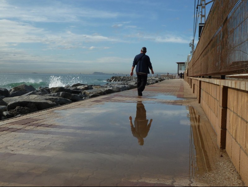 Un home al passeig entollat de Premià de Mar mentre el mar pica al mur de roques. G.A