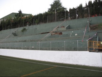 El camp de futbol de l'Arenys amb la gespa i la zona de les grades esllavissades amb el pavelló esportiu al fons. R.A