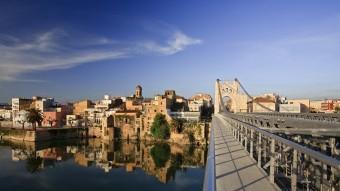 El pont penjant és un dels símbols de la ciutat, que es reflecteix en les aigües tranquil·les de l'Ebre. MARIANO CEBOLLA / PATRONAT TURISME AMPOSTA