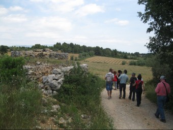 Un grup de persones passejant pel paisatge de la Garriga d'Empordà amb una barraca a l'esquerra. E. C