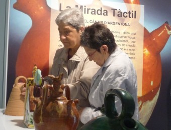 Dues dones toquen una de les peces del Museu del Càntir que integren l'espai tàctil que s'ha presentat aquest matí. T.M