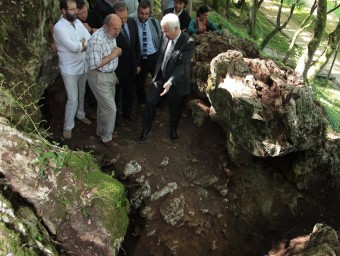 El crani, observat per Bibiana Agustí, Ferran Mascarell i Joaquim Soler. A la dreta, la cova on es van trobar les restes J. SABATER