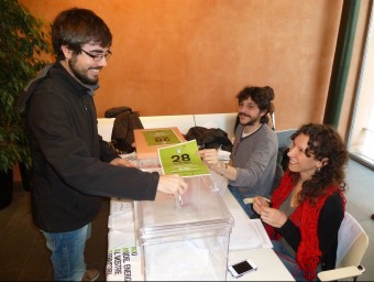 Un dels participants a la votació anticipada d'ahir a la biblioteca Vinyoli de Santa Coloma de Farners, amb Pera i Morell, a la mesa de les urnes. J.C
