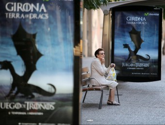 Una senyora asseguda en un banc entre anuncis de la sèrie que omplen Girona MANEL LLADÓ