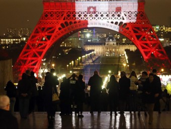 French police stand guard as people gather to look at the Eiffel Tower lit in the colours of the French flag, as part of a tribute to the deadly attacks that took place in the French capital./  REUTERS