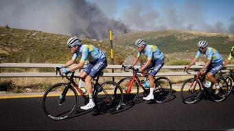 Un grup de ciclistes durant una etapa de la Volta a Portugal circulen amb l’incendi al fons