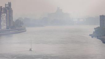 Un veler navega per l’East River de Nova York, sota el fum procedent dels focs del Canadà